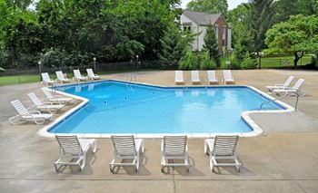 A swimming pool with chaise lounge chairs and trees in the background